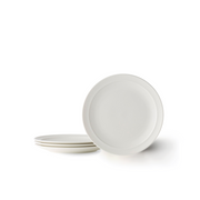 A set of four Adam Liaw Everyday Noritake medium white porcelain plates. One plate stands on its edge while the other three are stacked next to it on a white background.
