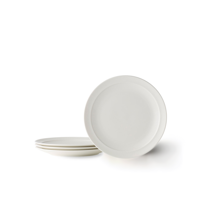 A set of four Adam Liaw Everyday Noritake medium white porcelain plates. One plate stands on its edge while the other three are stacked next to it on a white background.
