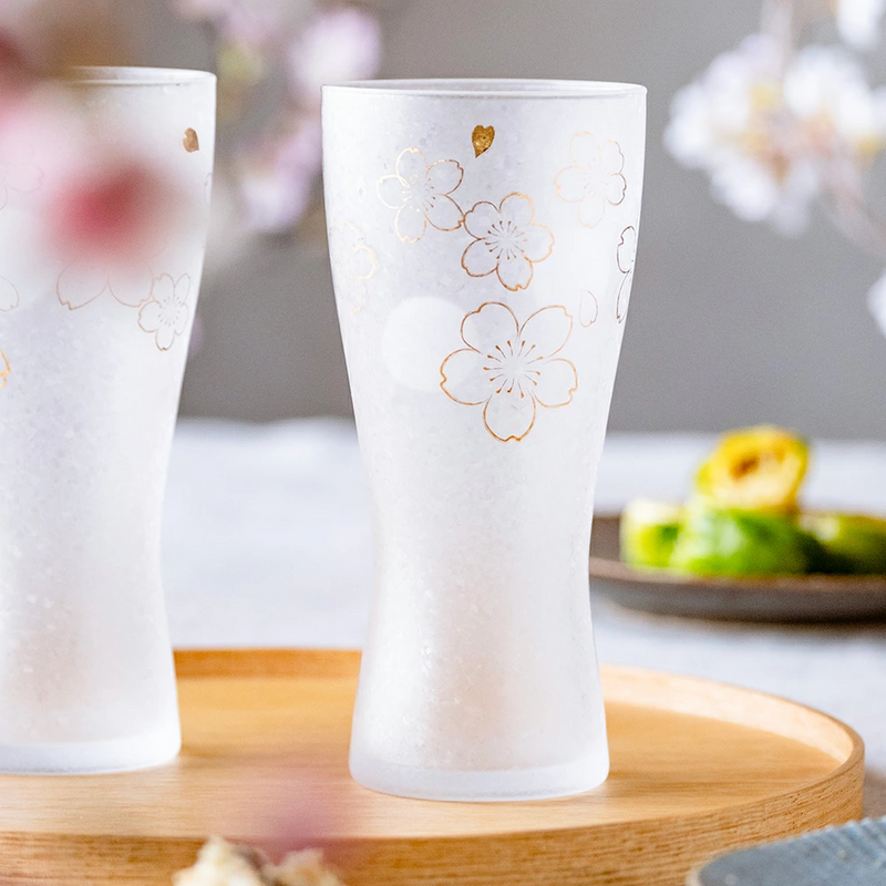 Two Aderia Sakura glasses on a wooden tray with soft floral background decor.

