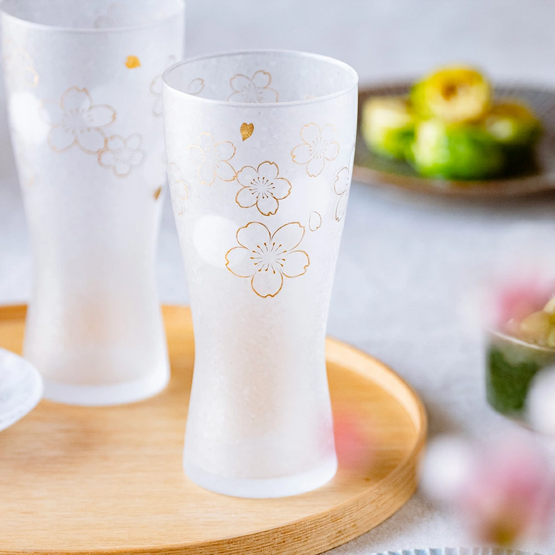 Aderia Sakura beer glass elegantly displayed on a wooden tray with food in the background.

