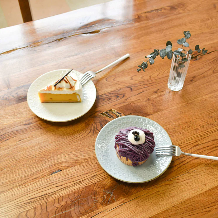 A close-up shot of a dessert plate from the Aito Mino Yaki Fog Series, showcasing a slice of cheesecake next to a cupcake with a purple swirl frosting.