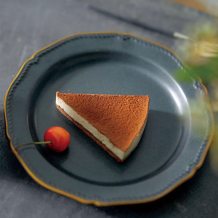 A matte black ceramic plate with scalloped edges, accented by a delicate gold trim, showcasing a single slice of tiramisu and a red cherry.