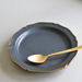 An overhead shot of the black ceramic plate, highlighting its unique scalloped design and gold trim, with a golden spoon resting on it.