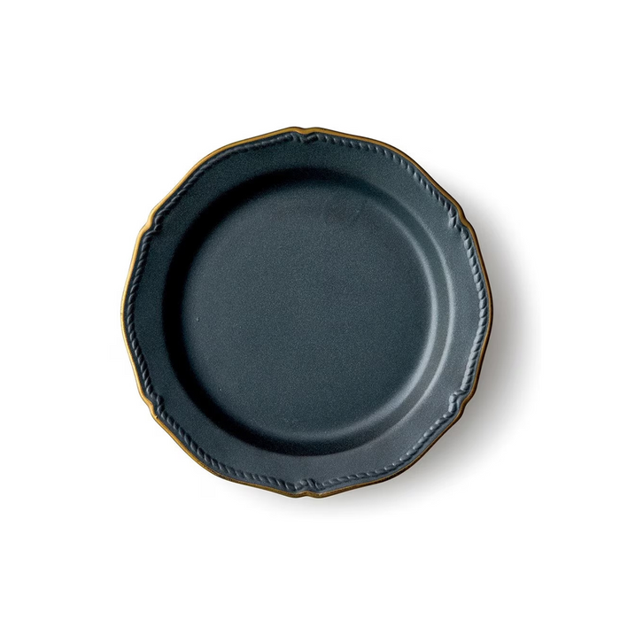 A matte black ceramic plate with intricately scalloped edges, accentuated by a subtle gold trim. The plate's surface displays a smooth finish with gentle curves.