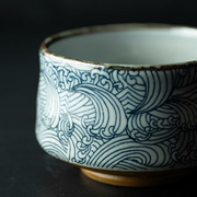 A close-up detail of the Arahami matcha bowl, showing the intricate blue and white 'wild wave' pattern and dark rim.