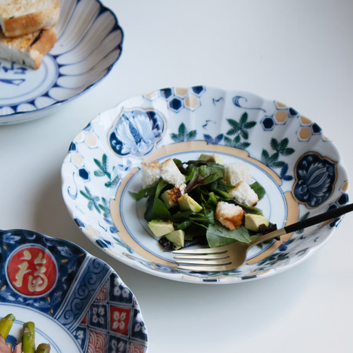 A large, deep white porcelain plate featuring an elegant pattern of green pine branches, blue flowers, and gold geometric accents.