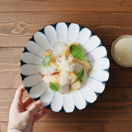 A large, deep white porcelain plate featuring bold blue radiating lines resembling a chrysanthemum and a central Japanese character for "Fortune" (Fuku).