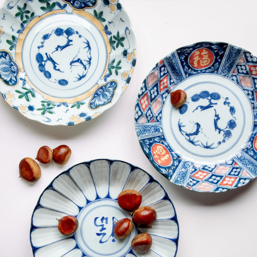 A set of three large Japanese plates featuring auspicious designs: one with a red and blue geometric pattern and 'Fuku' symbol, one with green and gold floral motifs, and one with blue radiating lines and a 'Fuku' symbol.