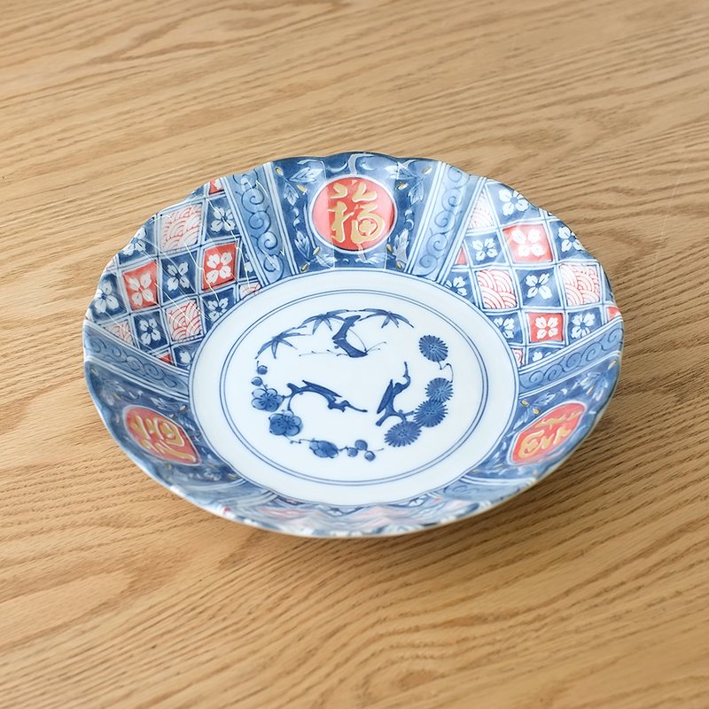A large, deep Japanese plate decorated with a traditional red and blue geometric lattice pattern and red circles containing gold "Fortune" symbols.