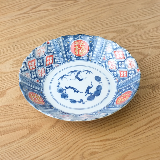 A large, deep Japanese plate decorated with a traditional red and blue geometric lattice pattern and red circles containing gold "Fortune" symbols.