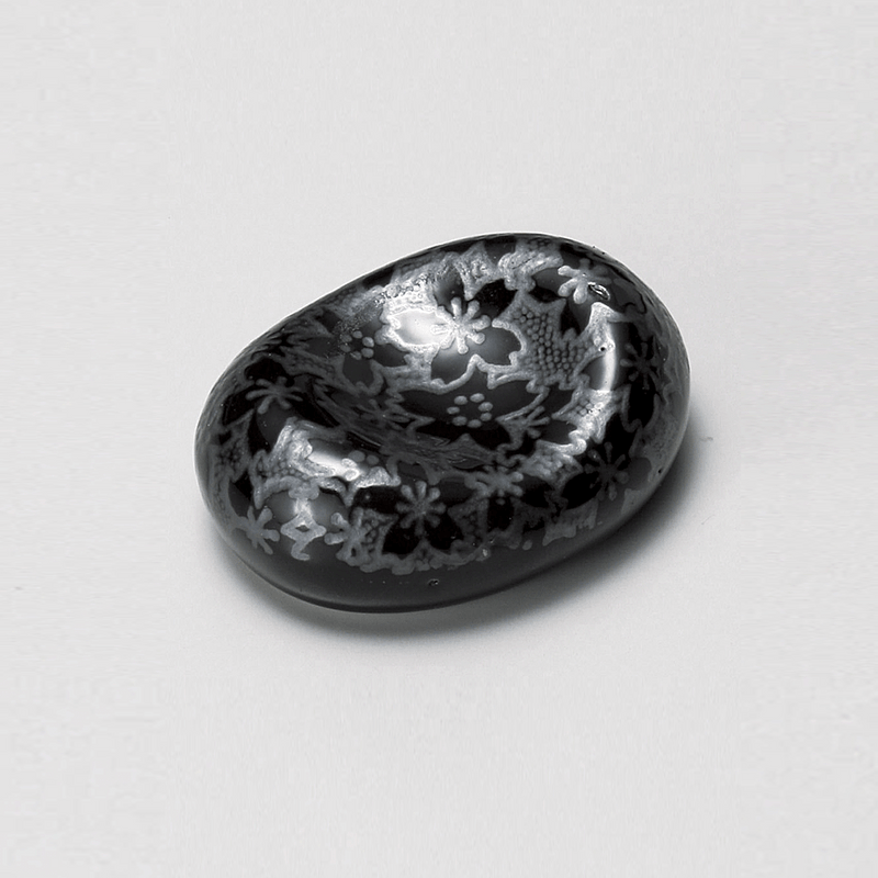 A Japanese porcelain chopstick rest with an organic shape, featuring a silver cherry blossom pattern on a black glaze.