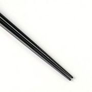 Tip view of glossy black chopsticks with finely tapered ends on white background.


