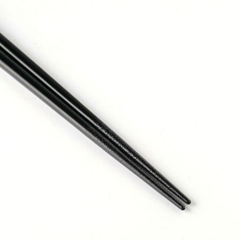 Tip view of glossy black chopsticks with finely tapered ends on white background.

