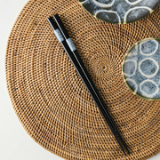 Black chopsticks with light blue circle pattern rests on a woven placemat alongside Japanese tableware.

