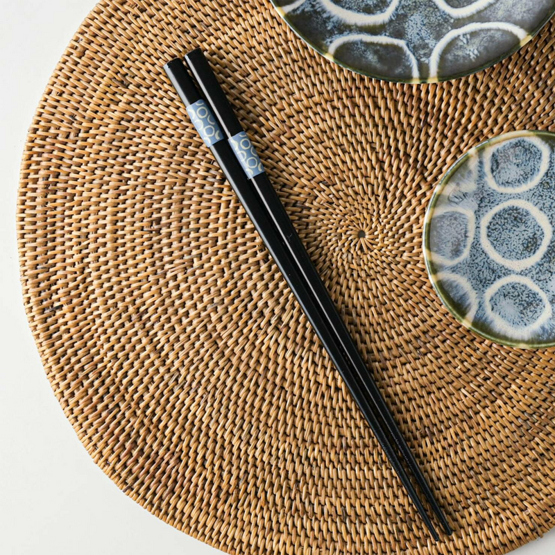 Black chopsticks with light blue circle pattern rests on a woven placemat alongside Japanese tableware.

