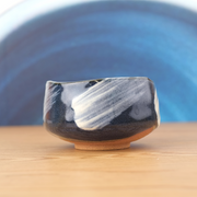 A styled photo of the blue and white brushstroke matcha bowl sitting on a wooden table, with a blue and white background. 