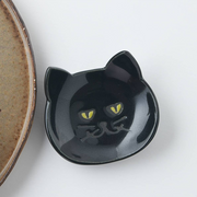 Close-up of a black Japanese cat cutlery rest with detailed facial markings and yellow eyes on a textured ceramic plate

