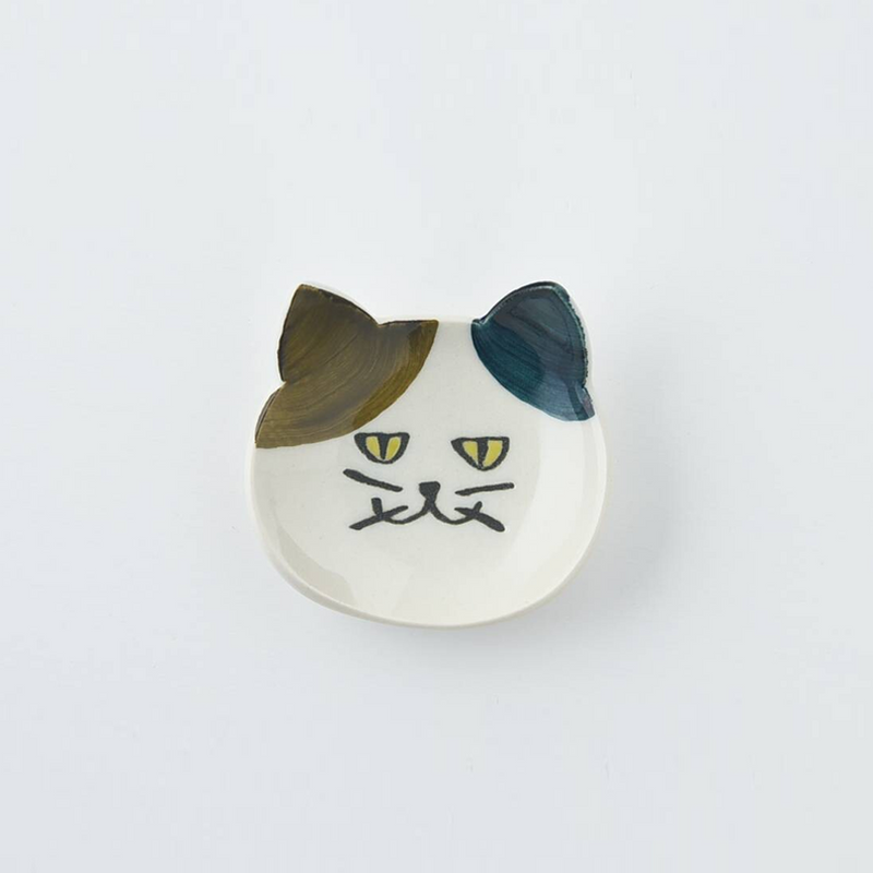 White Japanese cat cutlery rest with multicoloured ears on a textured ceramic plate.
