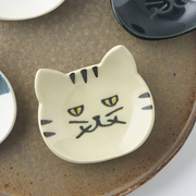 Cream-coloured Japanese cat cutlery rest displayed on a ceramic plate alongside other cat-themed cutlery rests
