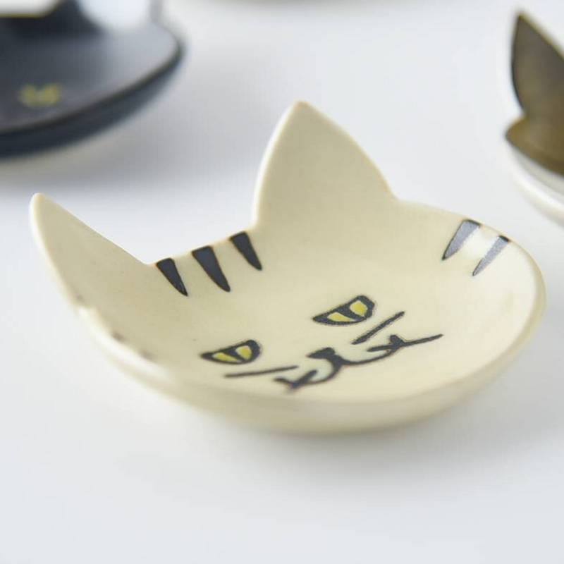 Close-up of a cream-coloured Japanese cat cutlery rest on a white surface, emphasizing its quaint facial markings
