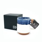 The CHIPS Stack Mug in White Navy Drop shown next to its elegant black gift box, with a branded tag attached to the handle.