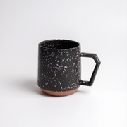 Two black CHIPS splatter mugs on a wooden table with a slice of cake and coffee-making equipment.