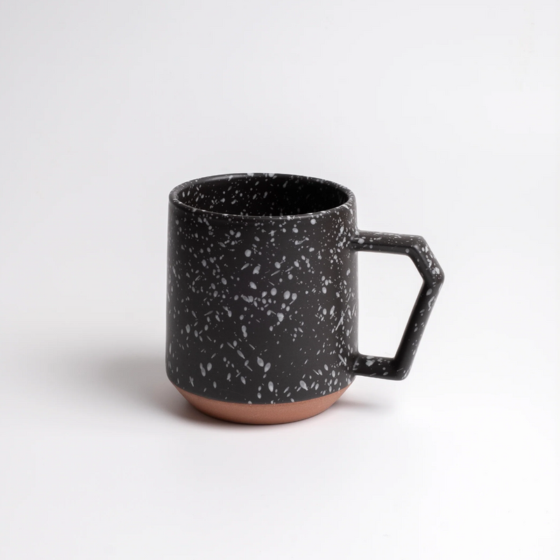 Two black CHIPS splatter mugs on a wooden table with a slice of cake and coffee-making equipment.