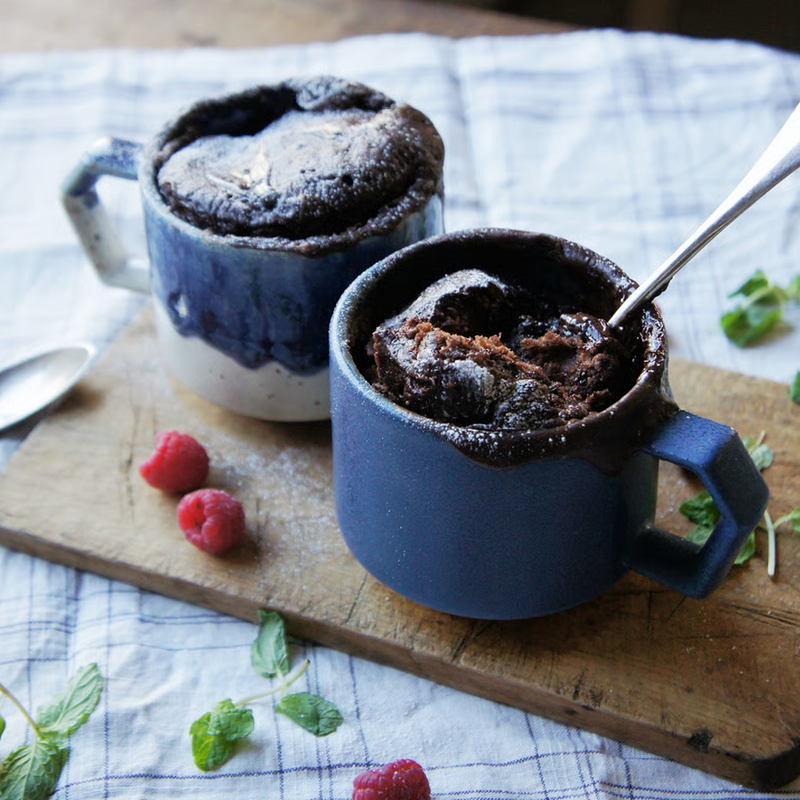 Two CHIPS mugs filled with chocolate mug cakes, garnished with raspberries and mint on a wooden board.