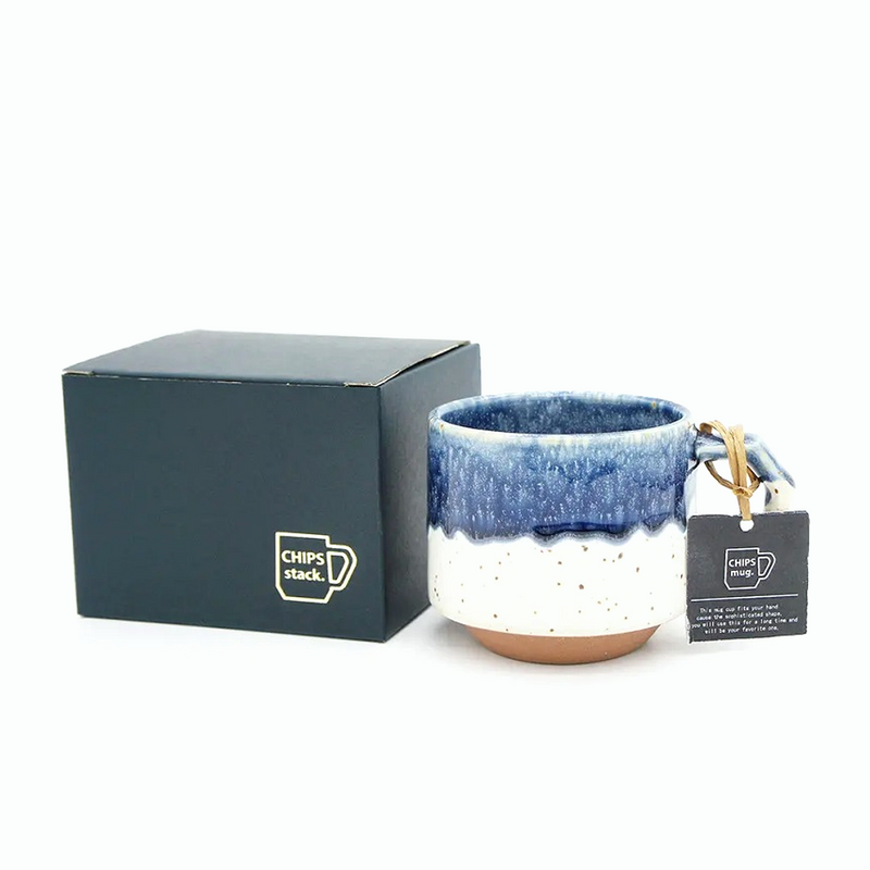 The 280ml CHIPS Stack Mug in White Navy Drop shown next to its elegant black gift box, with a branded tag on the handle.