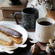A styled photo of two CHIPS mugs in different splatter colours, shown on a table with coffee and eclairs.