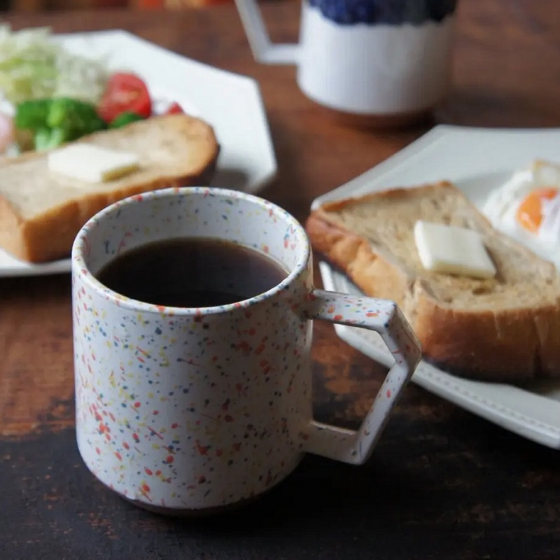 The CHIPS Stack Mug in Splash White Orange filled with coffee, shown as part of a breakfast setting with toast.
