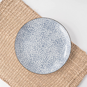 A Showa Seito Chrysanthemum plate with its intricate blue and white leaf pattern, displayed on a natural woven placemat.