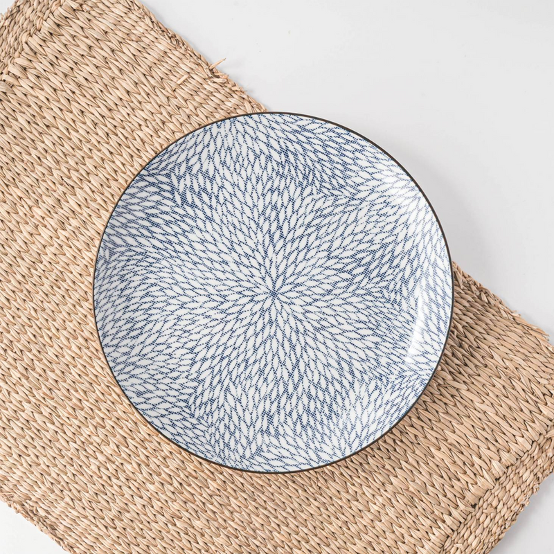 A Showa Seito Chrysanthemum plate with its intricate blue and white leaf pattern, displayed on a natural woven placemat.