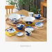 A beautifully arranged dining table featuring a set of Daitoua Neko Chigura tableware, including bowls, plates, and cups, each adorned with playful indigo cat illustrations on a white ceramic background, complemented by woven and fabric placemats.