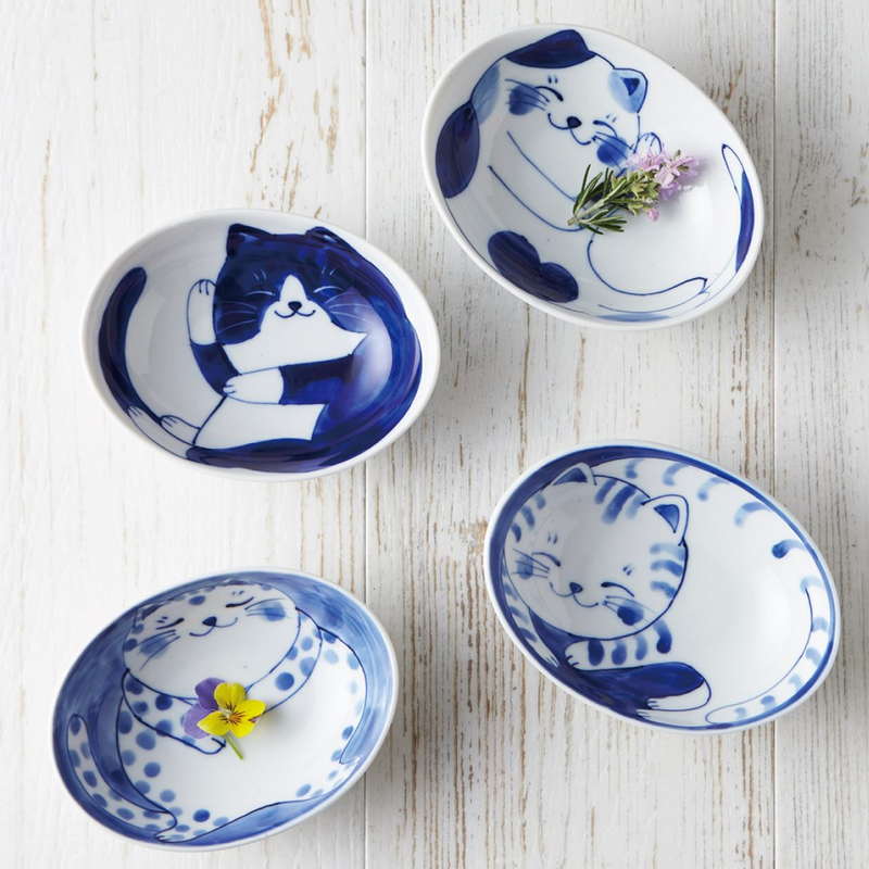 A collection of Daitoua Neko Chigura tableware featuring various cat illustrations, including oval serving bowls, plates, and small sauce dishes. The hand-painted blue and white designs showcase adorable cats in different playful poses.