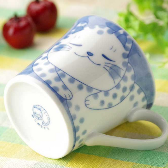 Top-down view of a white ceramic mug with blue cat design lying on its side, next to two cherry tomatoes.