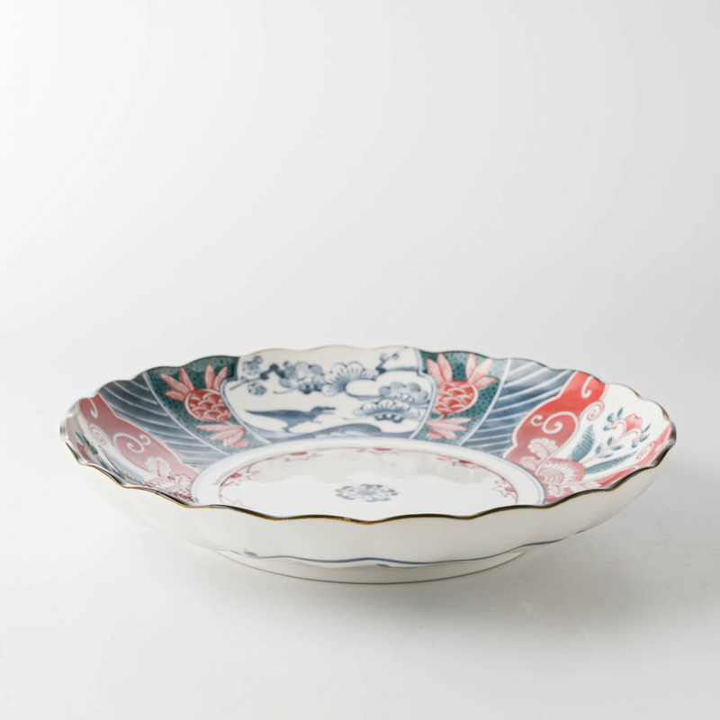 An angled view of the Edokko Dinosaur dinner plate, showing its scalloped rim and detailed red, blue, and green patterns.

