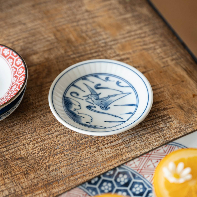 A lifestyle setting featuring the Edokko Dinosaur Hiyakuryu mini plate on a wooden table, displayed alongside other patterned dishes.