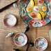 A collection of beautifully arranged mini plates featuring various dinosaur illustrations, set on a wooden table with sushi and chopsticks. The vibrant colors and patterns add a playful element to the dining setup.

