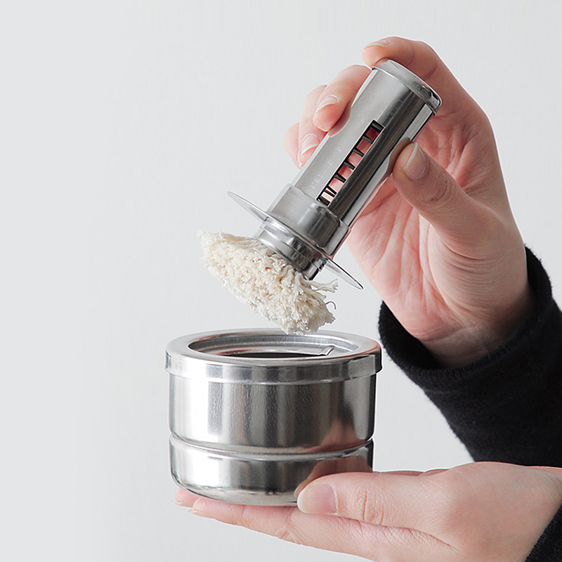 A person's hands holding the Freiz Stainless Steel Oil Basting Set, with the fabric brush being dipped into the oil pot.
