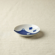 A small round porcelain side plate featuring a deep indigo Mount Fuji and plover bird motif on a white background, placed on a neutral cloth backdrop.







