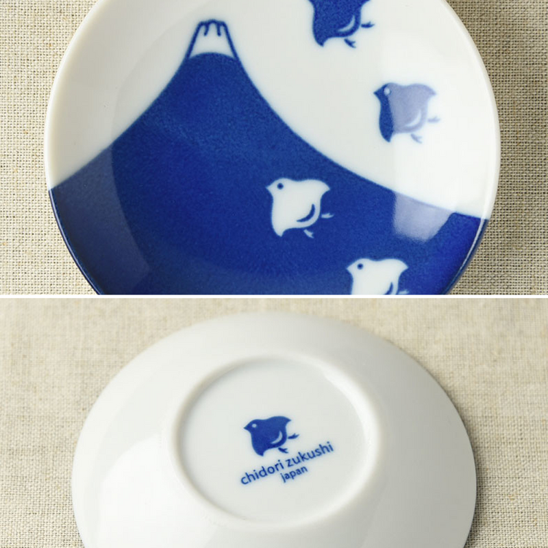 A close-up of a small round porcelain side plate showcasing the Mount Fuji and plover bird design on the top, and the blue chidori zukushi Japan logo on the underside.






