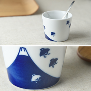 Close-up view of a white ceramic cup showing detailed blue Mount Fuji and bird designs with a utensil resting inside, highlighting its use as a food container.