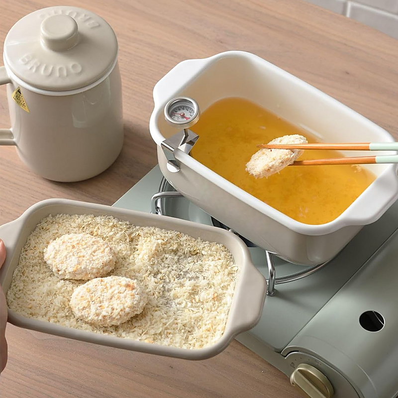 The Fuji deep fryer in use on a portable stove, with food being breaded in one tray and fried in the main pot.