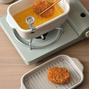 Lifting a golden-brown Japanese croquette from the Fuji deep fryer, with another piece resting on the draining rack.
