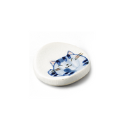 A Japanese porcelain chopstick rest with a crackle glaze, showing a hand-painted illustration of a sleeping blue cat.