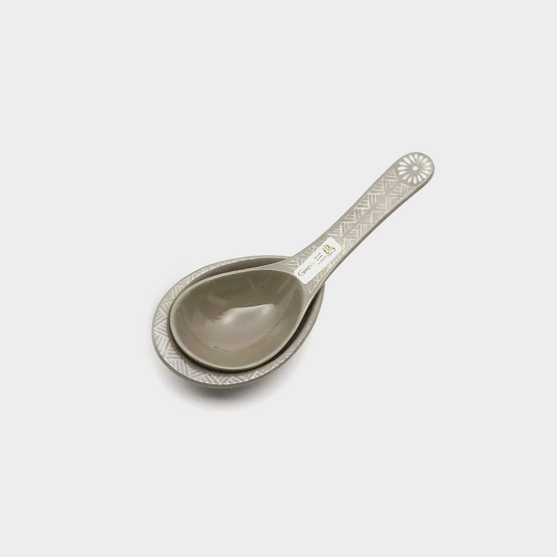 A silver-colored metal spoon with a floral pattern on the handle, accompanied by a matching spoon rest.