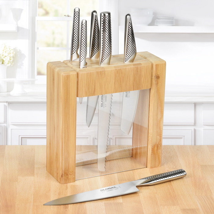 Global Ikasu 7-piece knife set in a bamboo and acrylic knife block on a kitchen countertop.