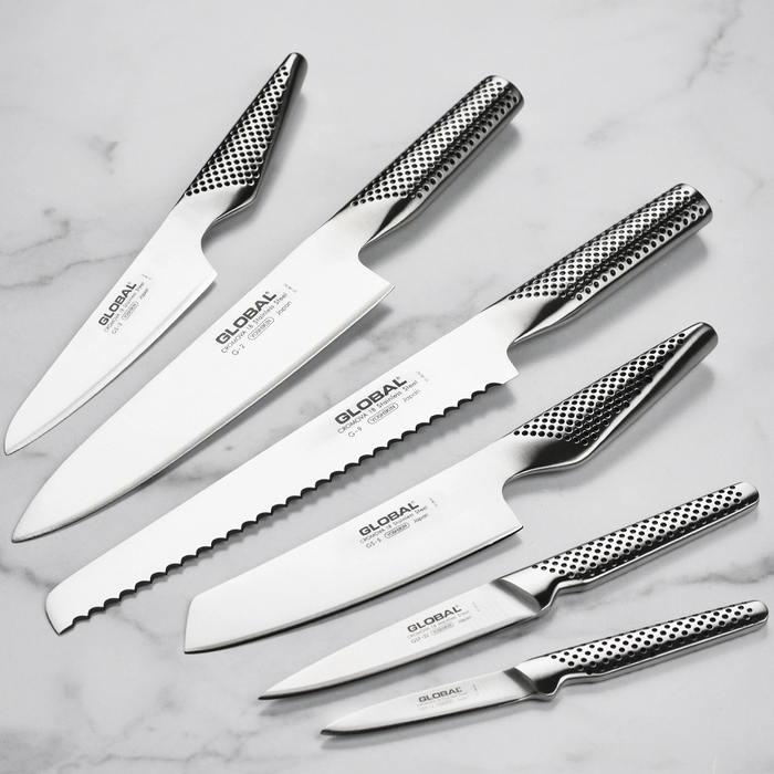 Six Global Ikasu knives arranged on a marble surface, showcasing their sleek design and sharp blades.