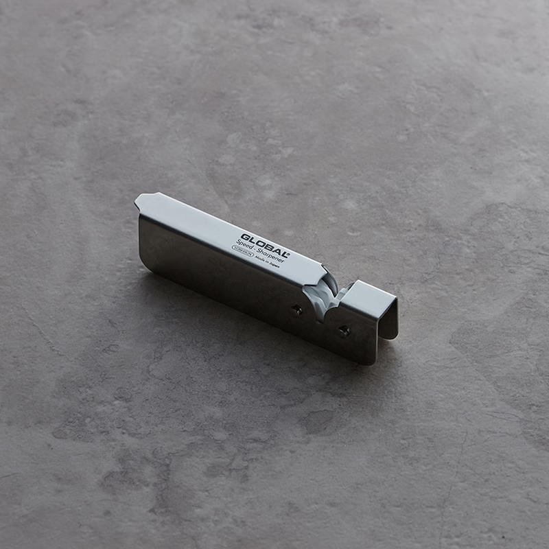 The stainless steel Global Speed Sharpener resting on a dark, textured surface.